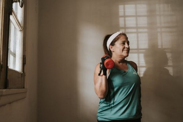 Middle-aged woman in workout attire lifting a dumbbell indoors, promoting fitness and healthy lifestyle.
