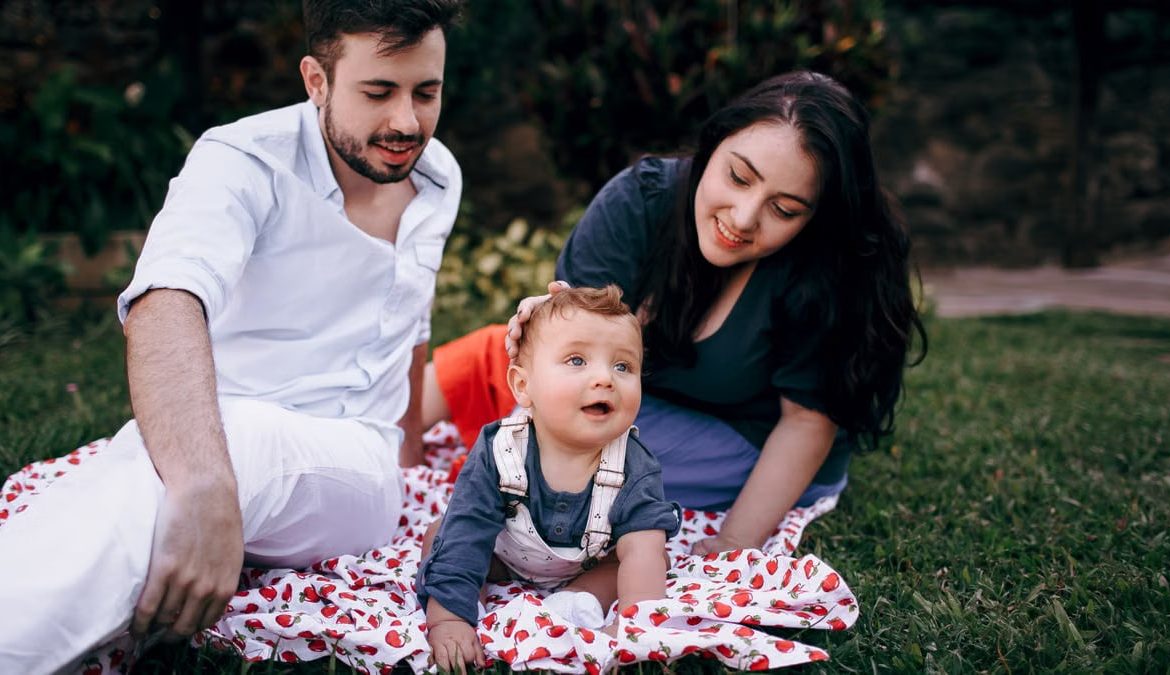 A joyful family enjoying a picnic outdoors during summer. Smiling parents with their baby on a blanket.