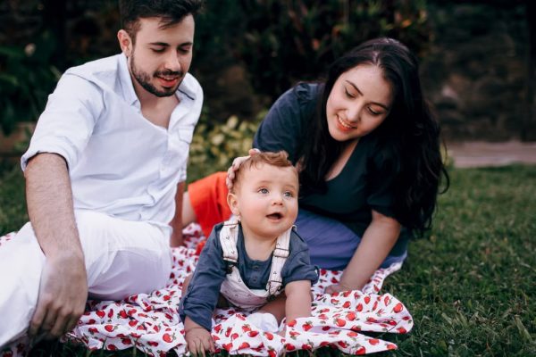 A joyful family enjoying a picnic outdoors during summer. Smiling parents with their baby on a blanket.