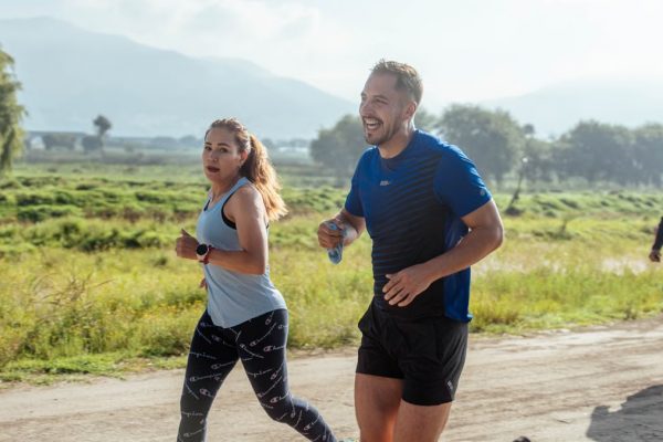 Two adults running on a rural dirt path, enjoying a sunny day outdoors.